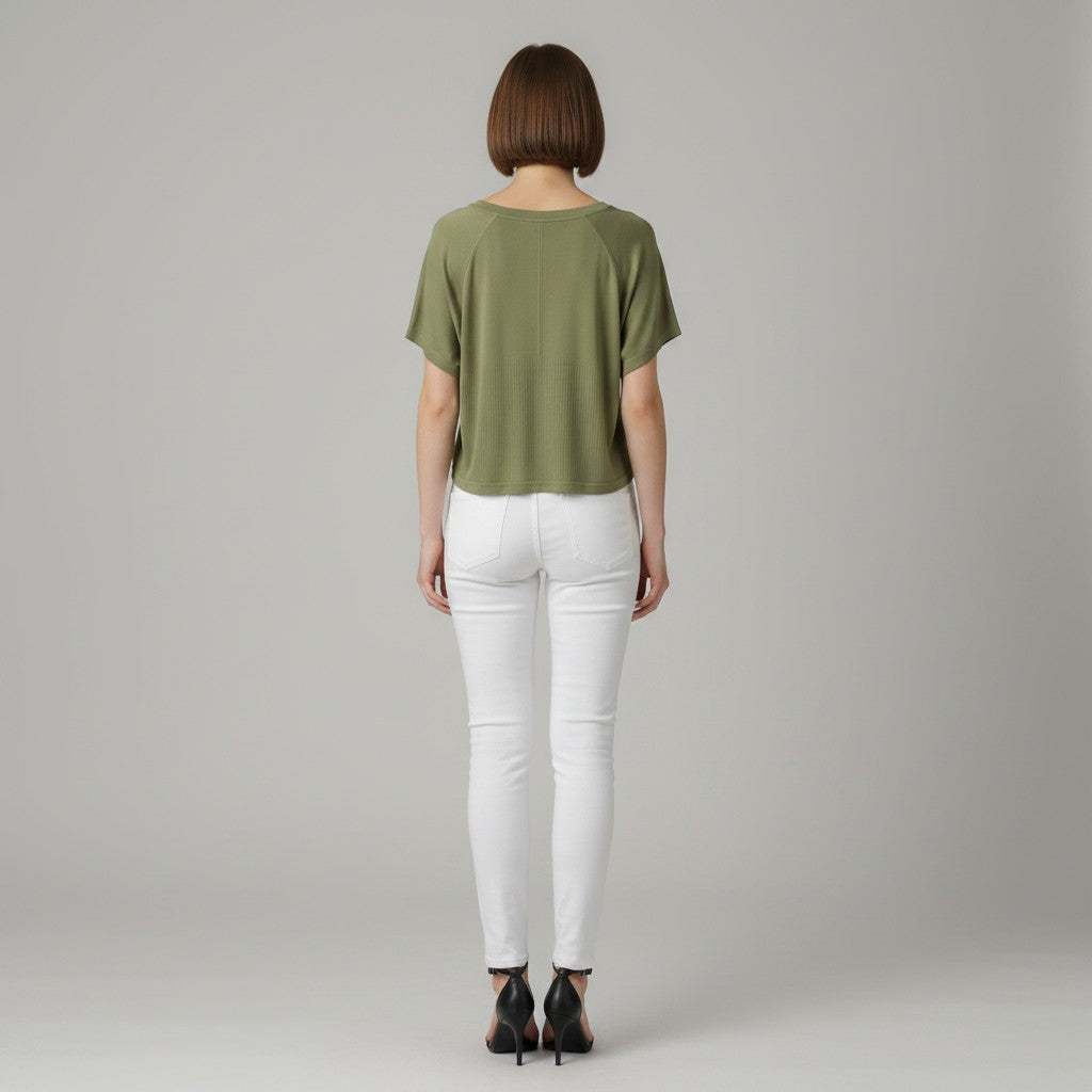 A woman wearing a green shirt, white jeans, and black high heels on a studio gray background.