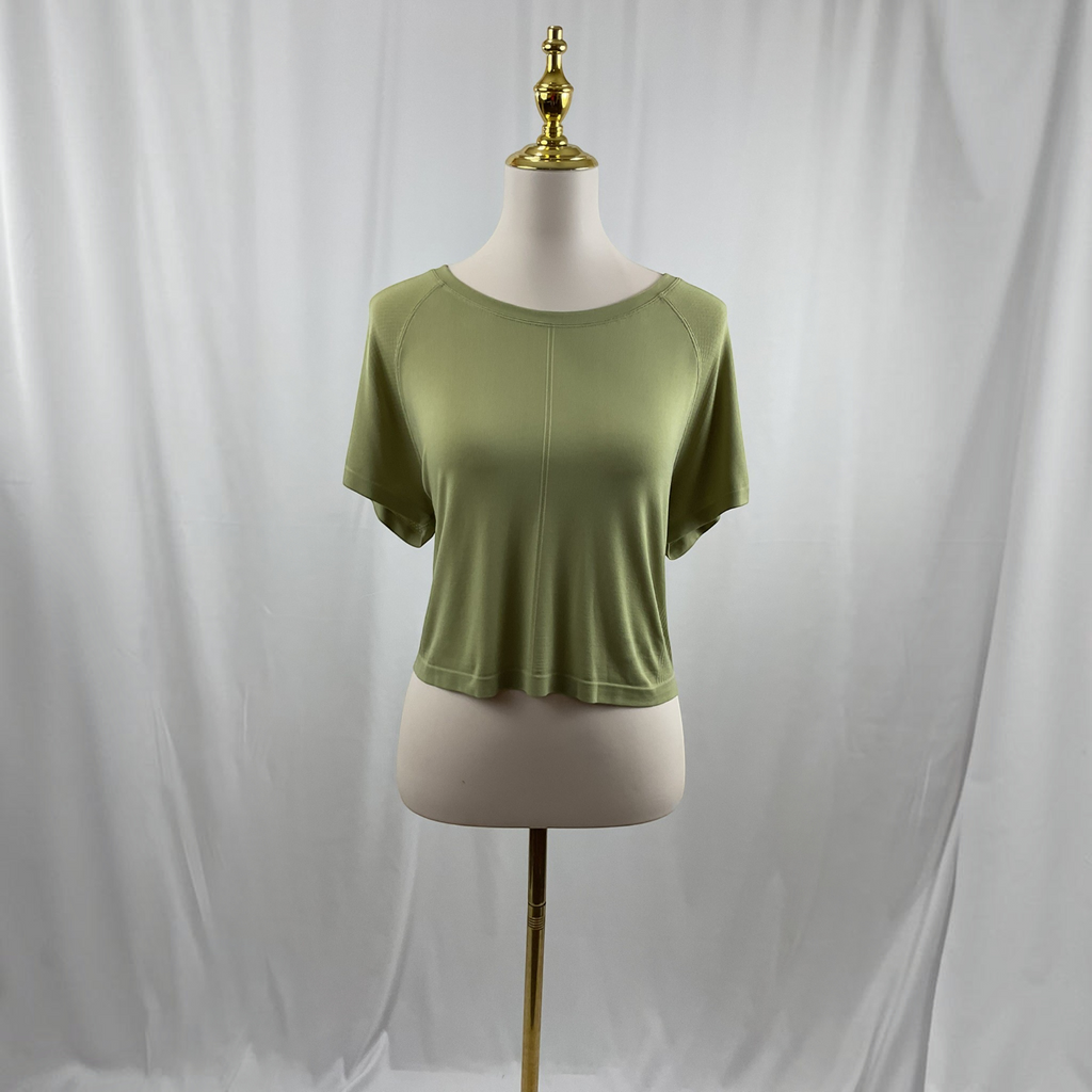 A woman wearing a green shirt, white jeans, and black high heels on a studio gray background.
