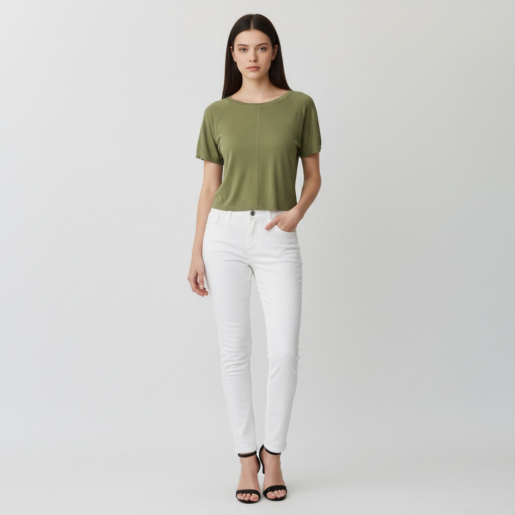 A woman modeling a short-sleeve olive green top and white skinny jeans with black high-heeled sandals, standing against a light gray studio background.