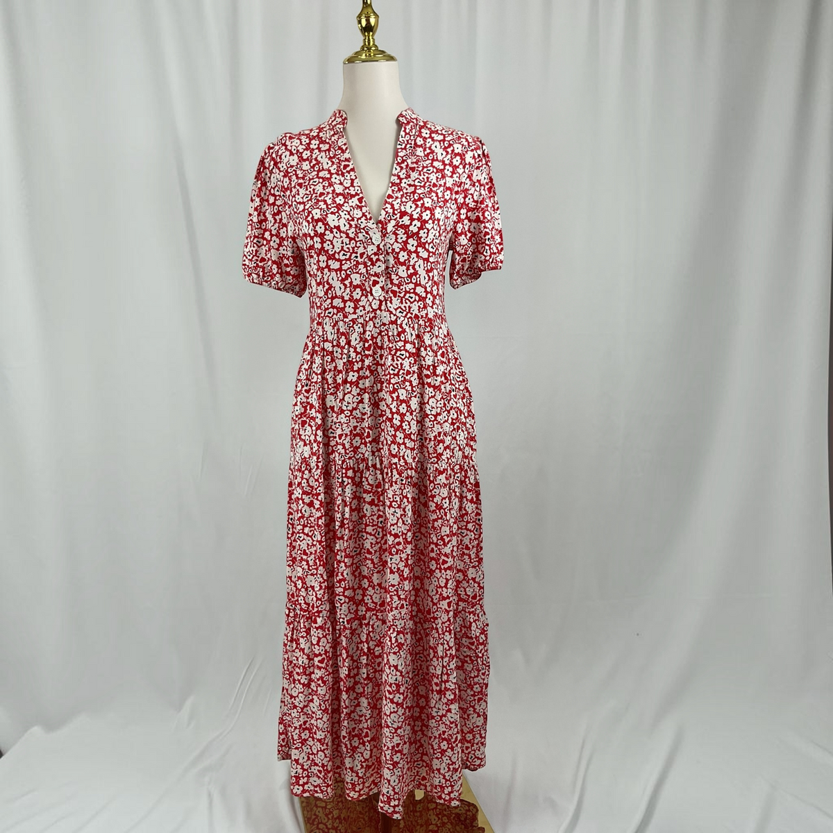 A woman in a red and white short sleeve dress and black heels on a light gray studio background.