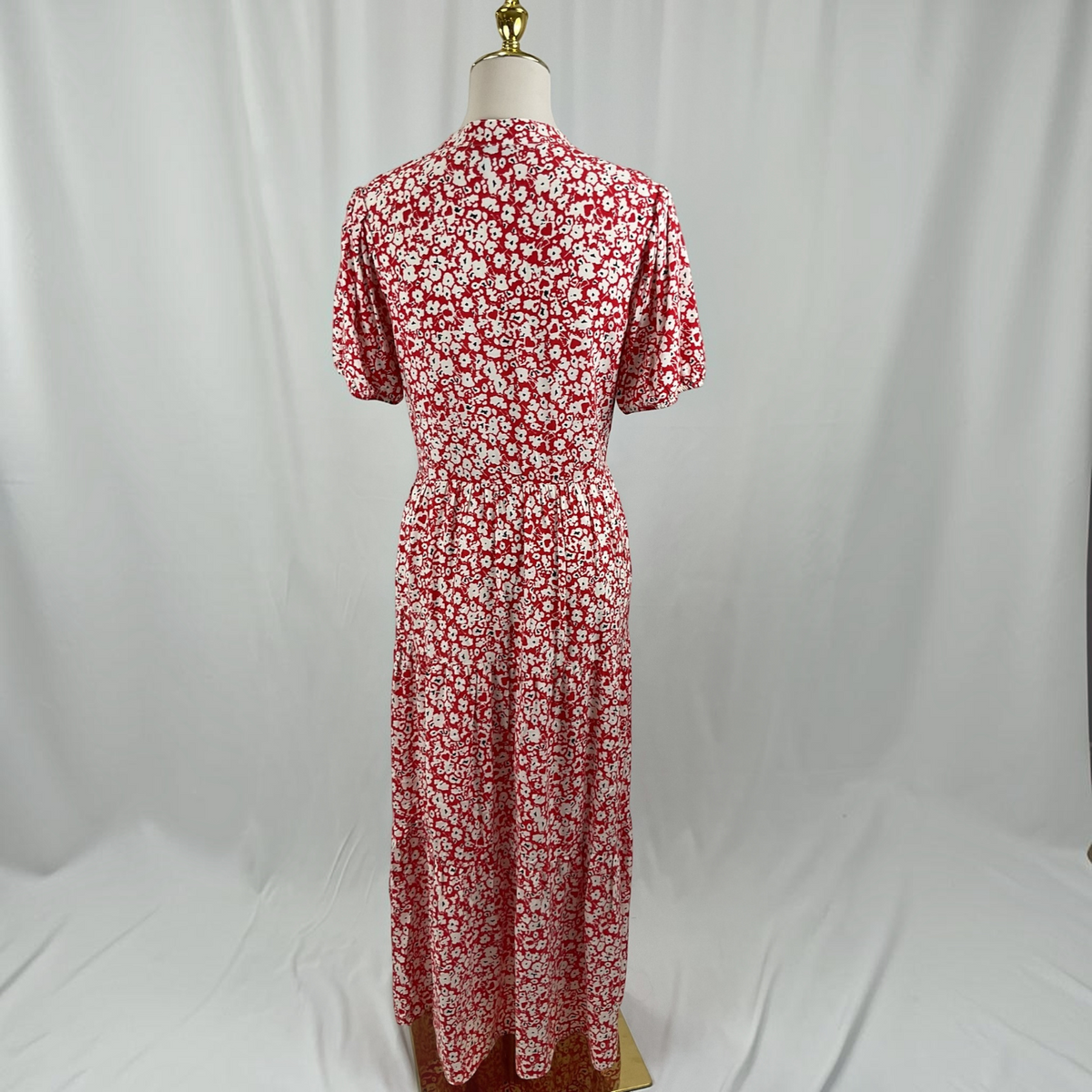 A woman in a red and white short sleeve dress and black heels on a light gray studio background.