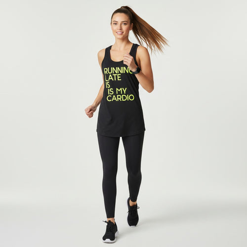 A woman running in a black athletic tank top with yellow text reading 'RUNNING LATE IS MY CARDIO' and black leggings, photographed against a clean light gray studio background.
