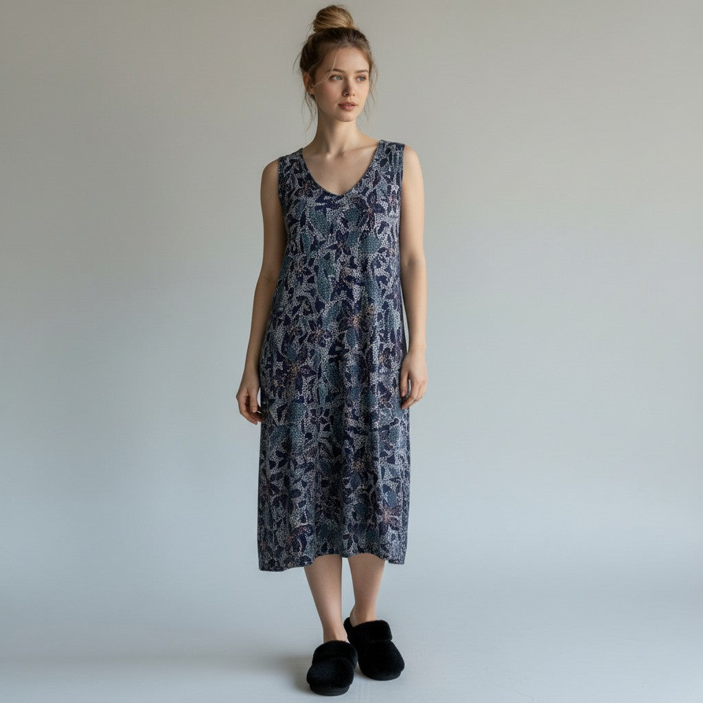 A woman wearing a floral print dress with no sleeves and black fuzzy slippers on alight gray studio background.