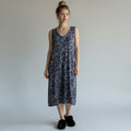 A woman wearing a floral print dress with no sleeves and black fuzzy slippers on alight gray studio background.
