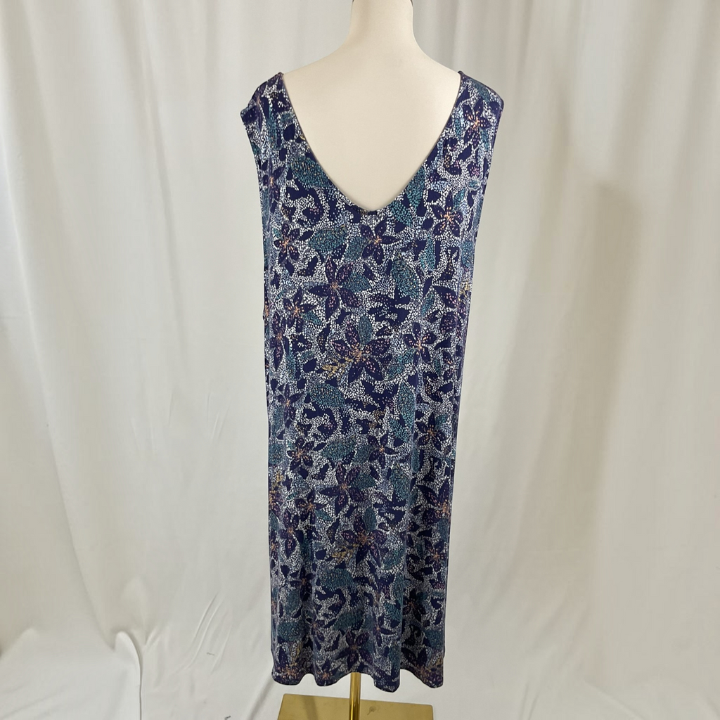 A woman wearing a floral print dress with no sleeves and black fuzzy slippers on alight gray studio background.