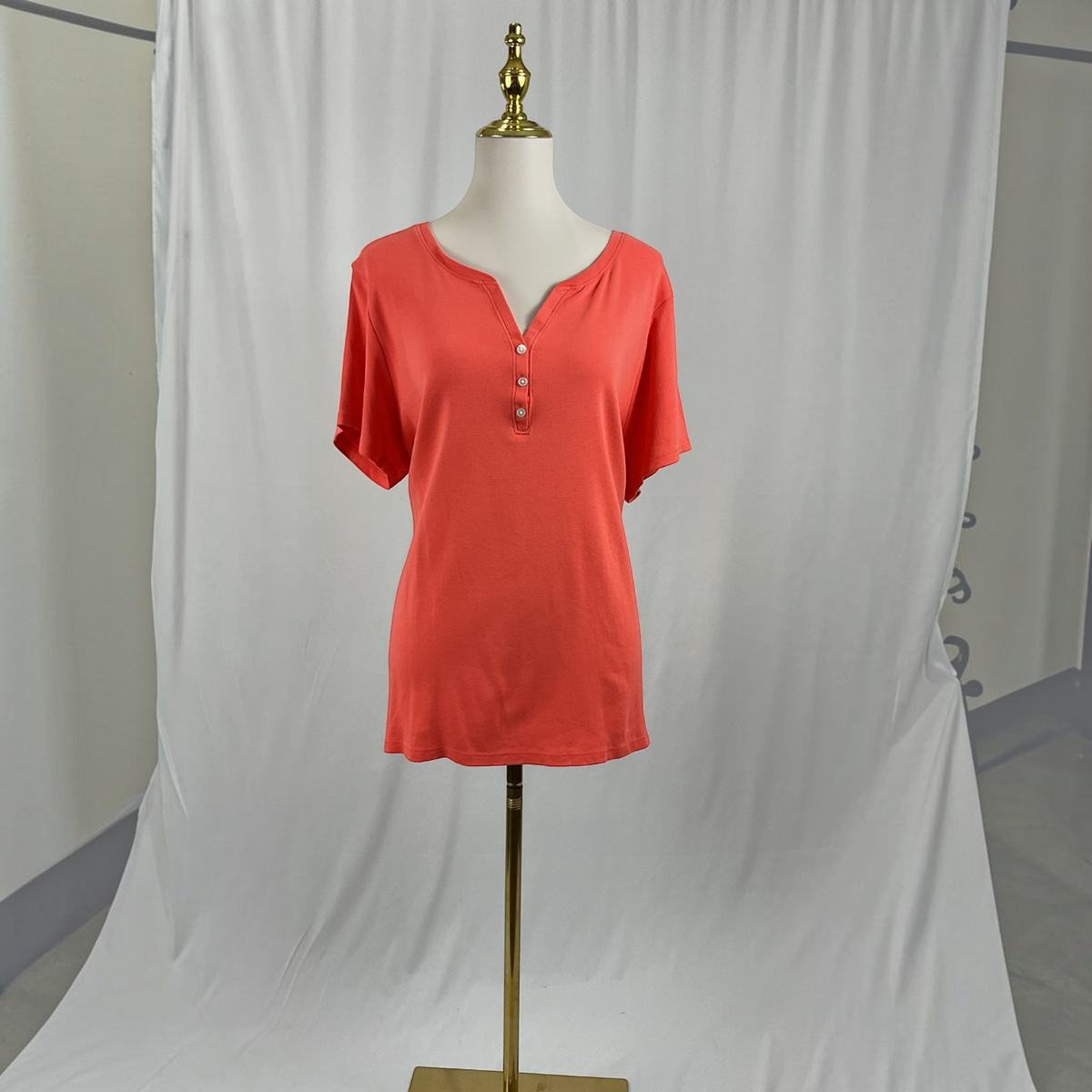 A woman with a coral shirt, white jeans, black high heels on a studio gray background.