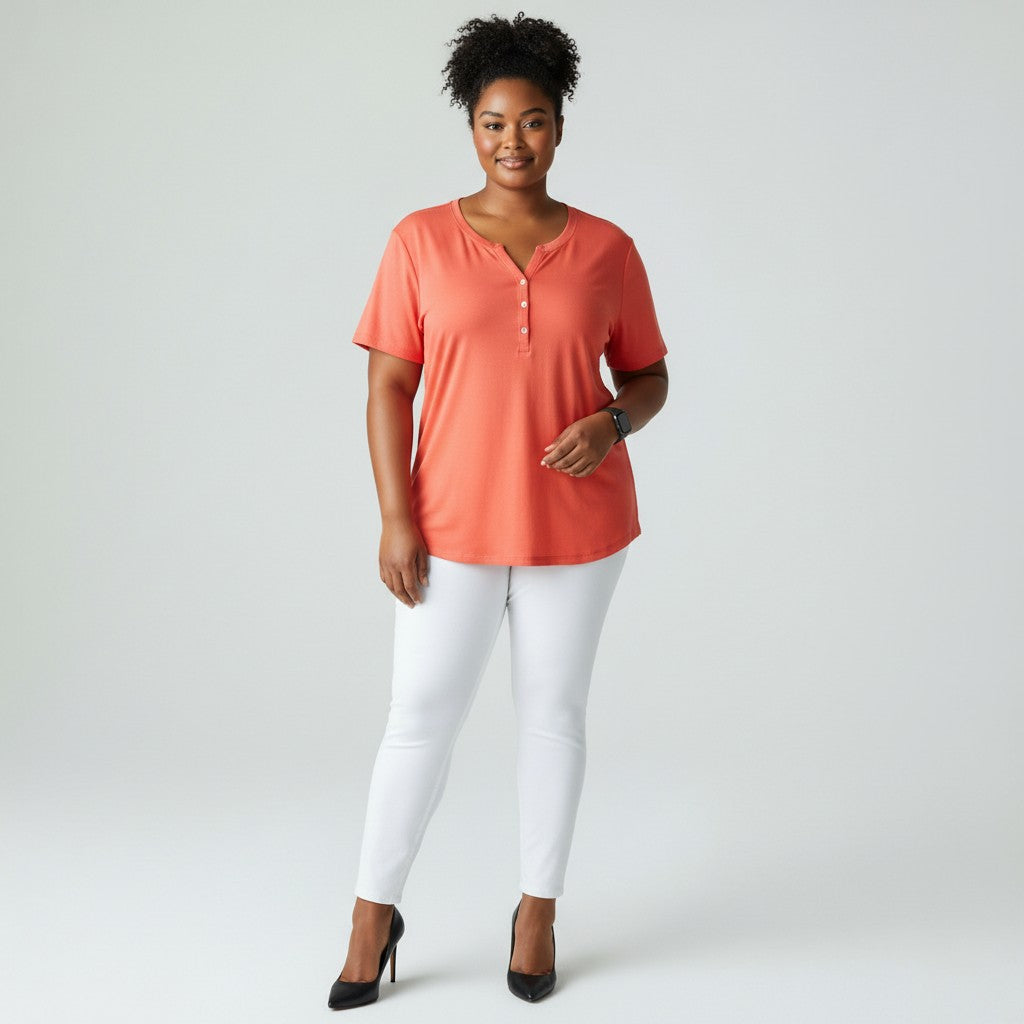 A woman with a coral shirt, white jeans, black high heels on a studio gray background.