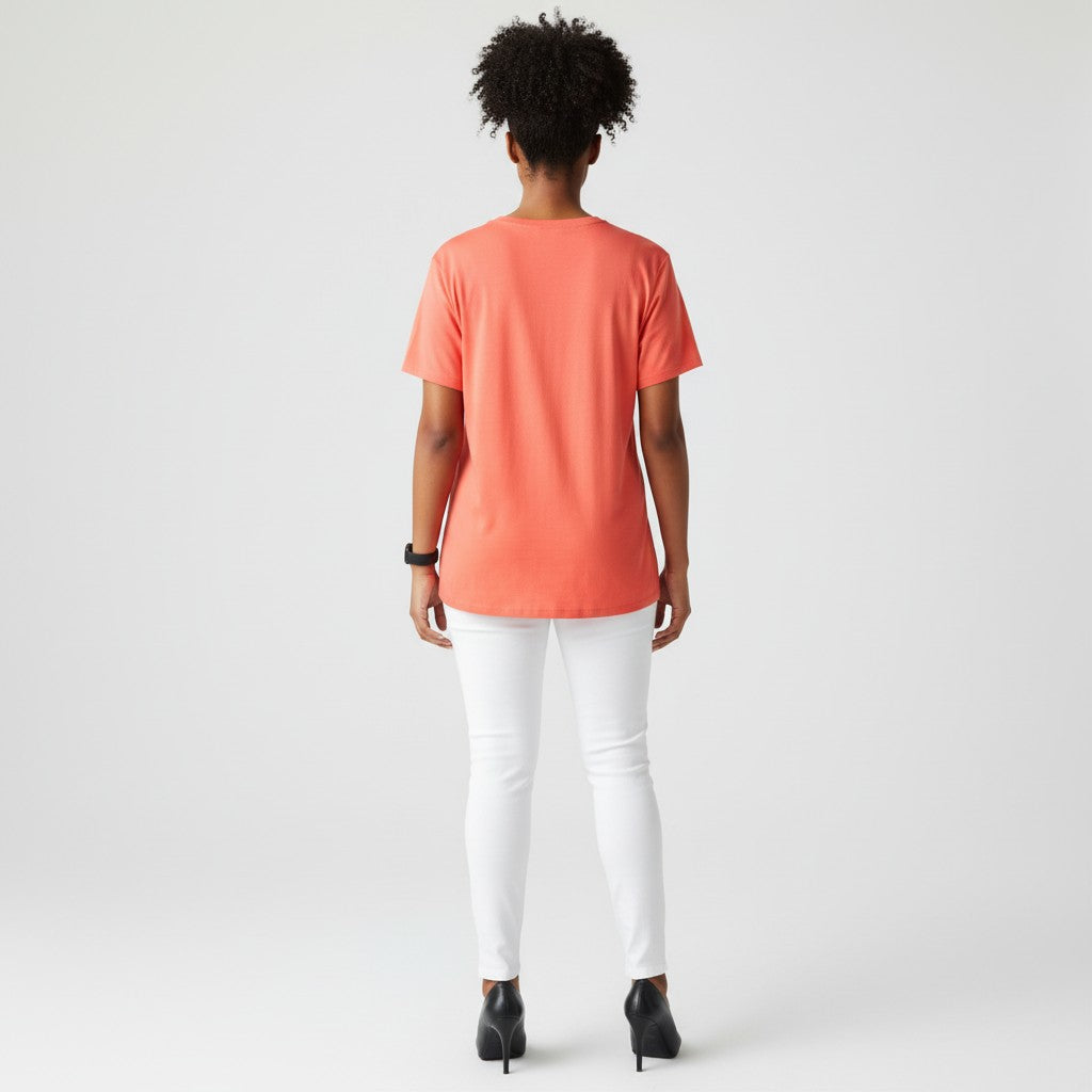A woman with a coral shirt, white jeans, black high heels on a studio gray background.