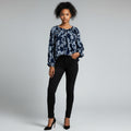 A woman with a blue and navy long sleeve shirt , black jeans , black high heels on a studio gray background.
