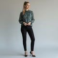 A woman wearing a floral top, black skinny jeans, black high heels on a studio background