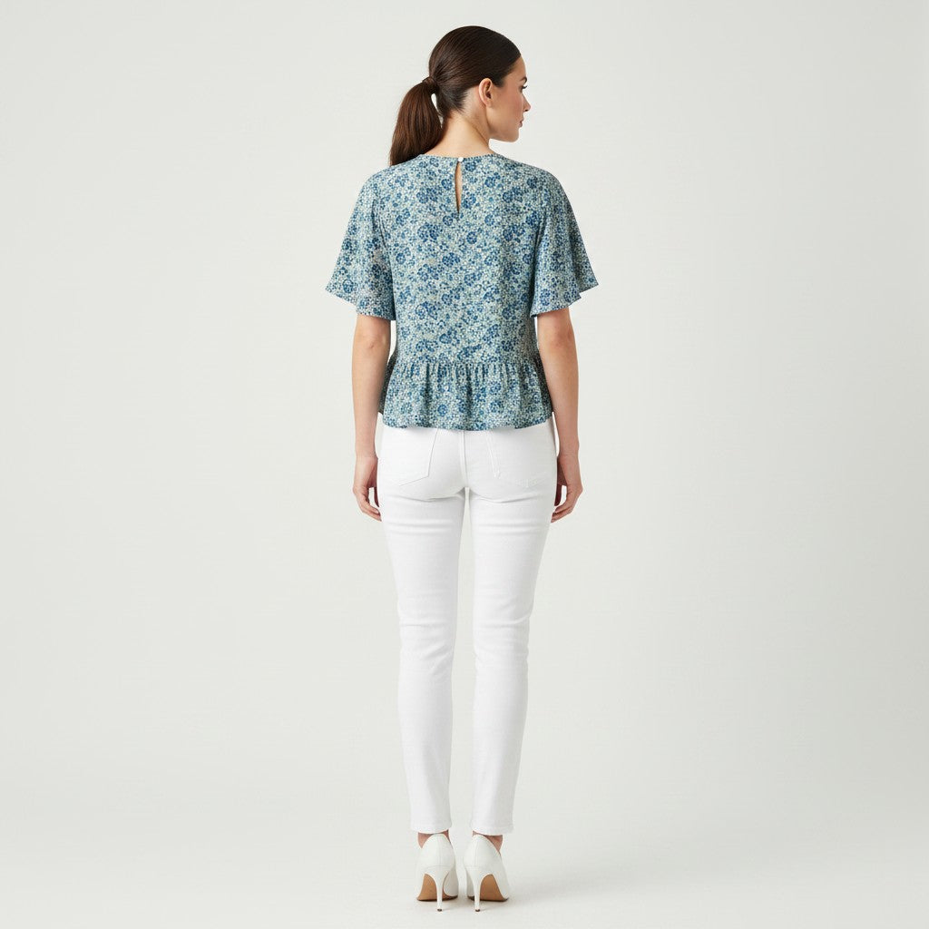 A woman wearing a floral top, white jeans, white high heels on a studio gray background.