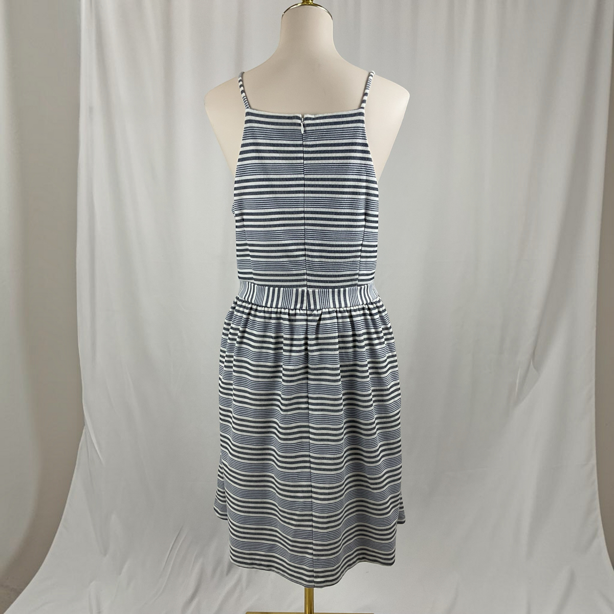 A sleeveless spaghetti-strap dress with a fitted bodice and flared skirt, featuring horizontal navy and white stripes, displayed on a mannequin against a draped white fabric backdrop.