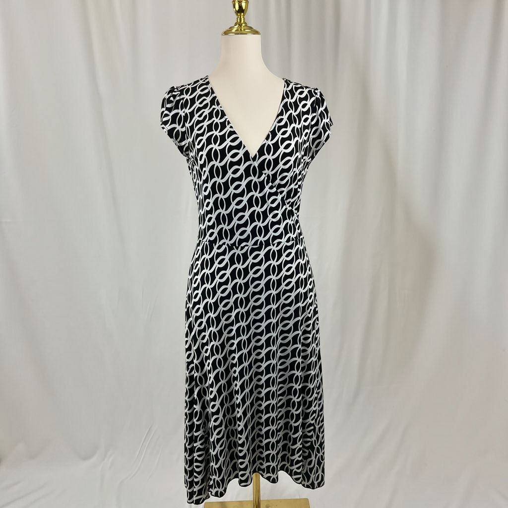 A black and white patterned shift dress with a V-neckline and cap sleeves, displayed on a mannequin against a white draped fabric background.