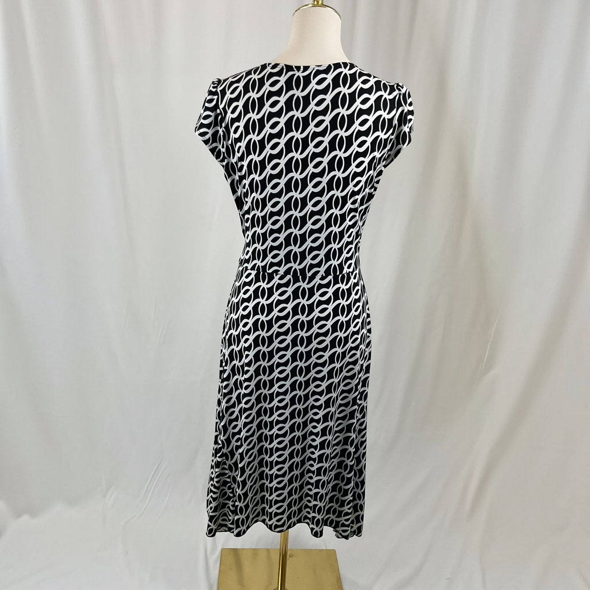 A black and white patterned knee-length dress displayed on a mannequin against a white draped fabric backdrop.