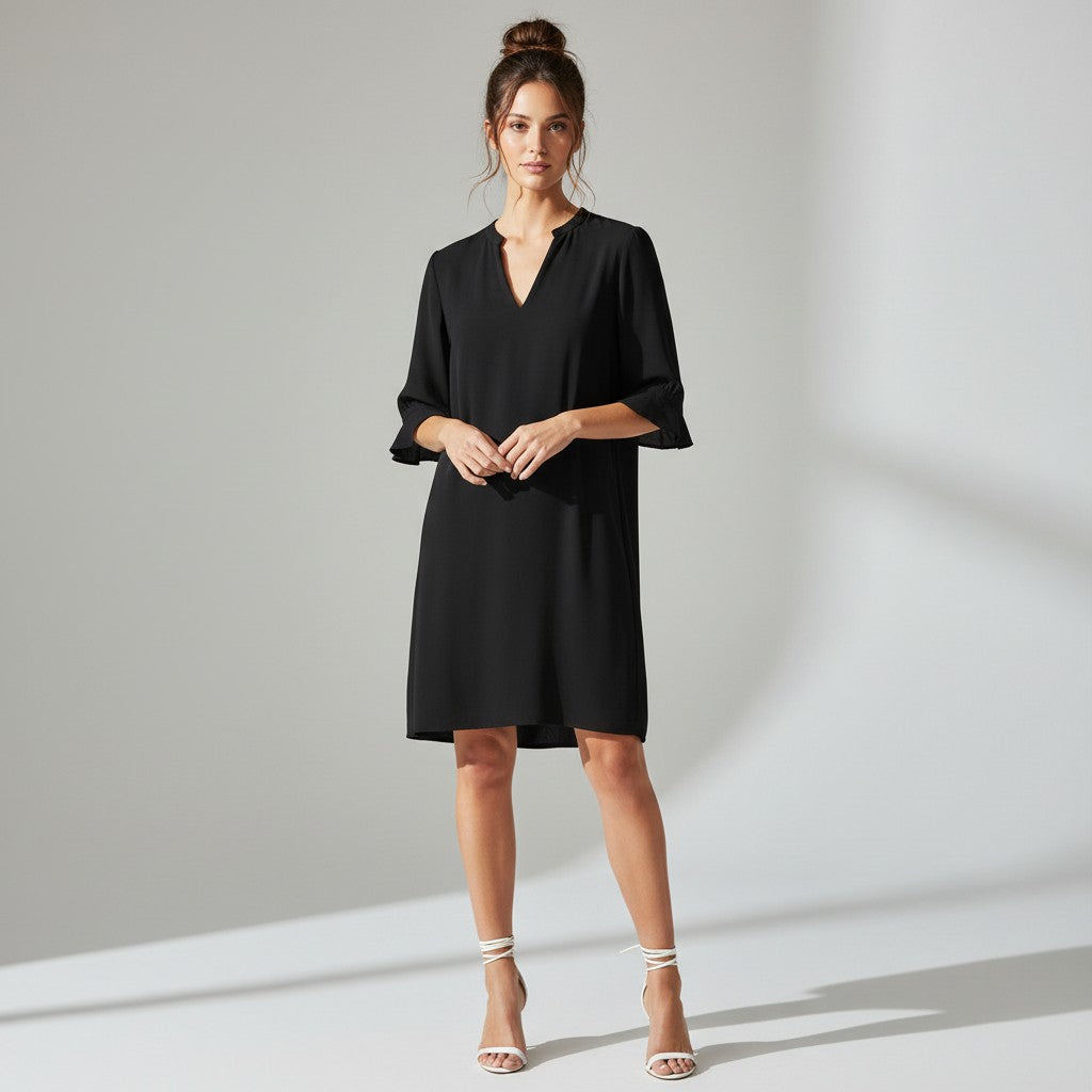A woman modeling a black short-sleeve V-neck dress with elbow-length flared sleeves, standing against a light gray studio background with soft shadows.