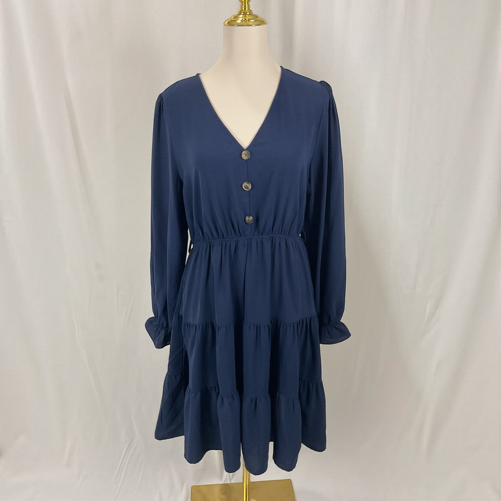 A navy blue tiered dress with long sleeves and a buttoned V-neckline, displayed on a mannequin against a white fabric backdrop.