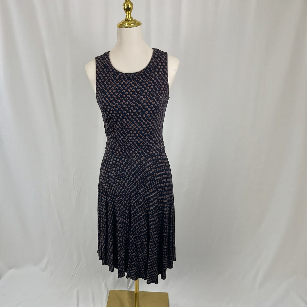 A sleeveless fit-and-flare dress with a small repeating geometric pattern in dark navy and pink, displayed on a white mannequin with a gold finial against a white fabric backdrop.