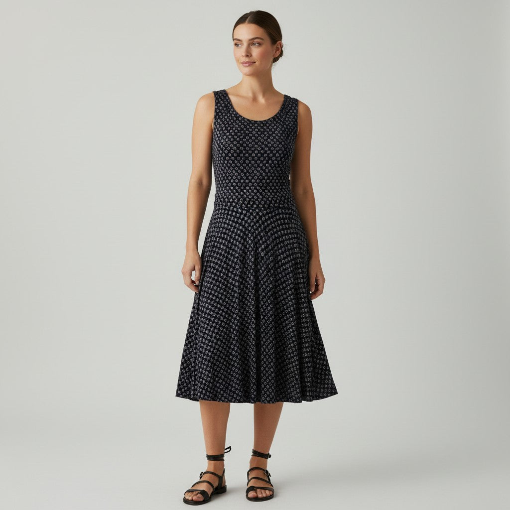 A woman modeling a sleeveless midi dress with a black and white micro-dot pattern, standing against a light gray studio background.