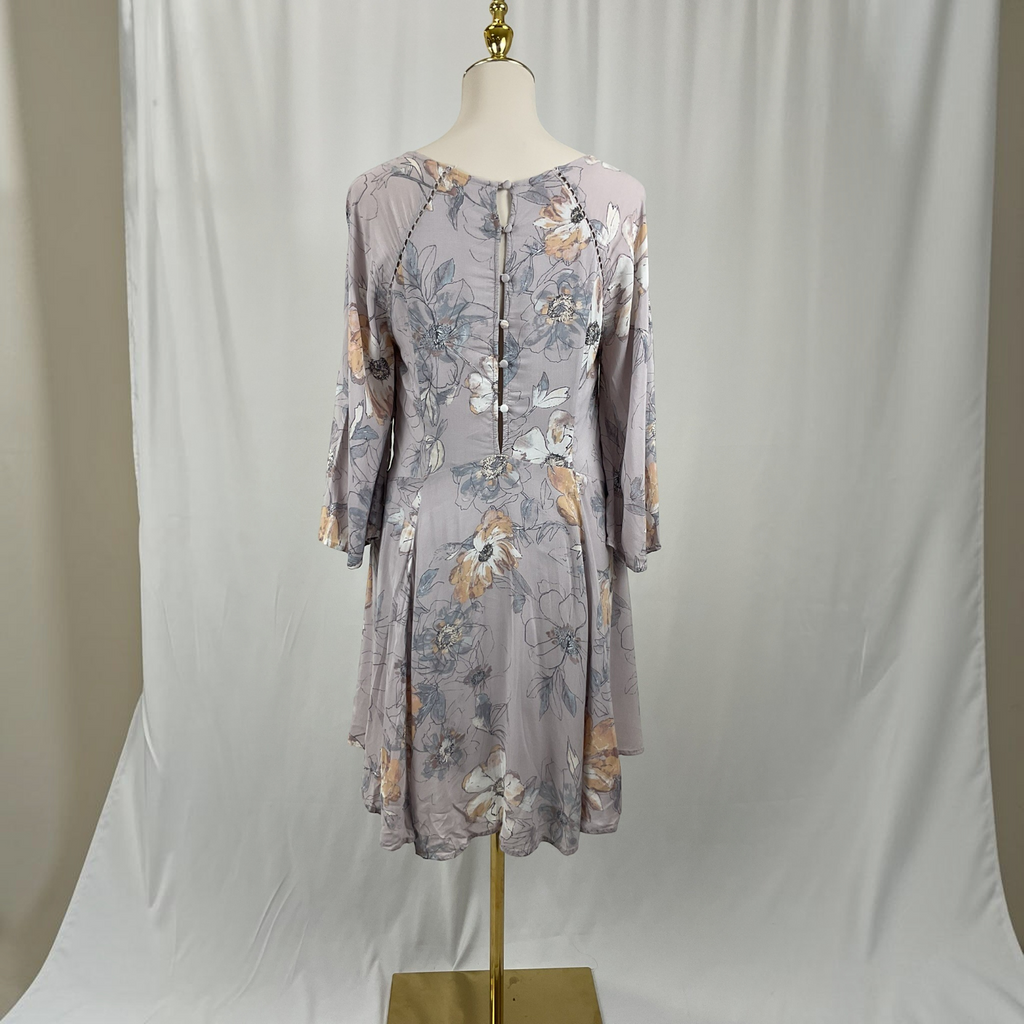 A three-quarter sleeve floral dress in a dusty lavender-gray color, displayed on a mannequin torso with a gold stand against a white fabric backdrop.