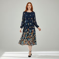 A woman modeling a long-sleeve midi dress with a dark navy base and a colorful butterfly and floral print, set against a neutral light gray studio background.