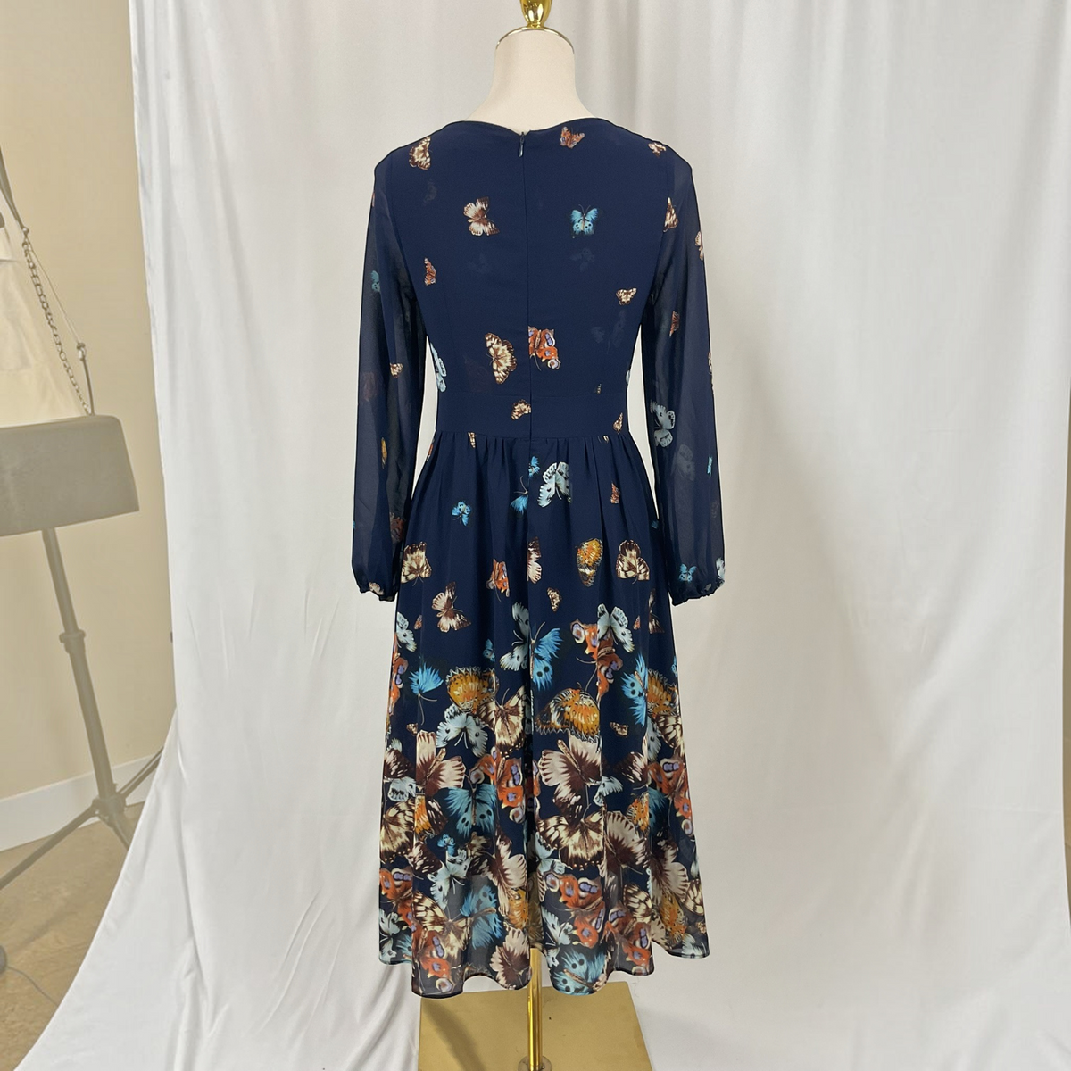 A navy blue long-sleeve midi dress with a colorful butterfly and floral print, displayed on a mannequin in front of a white studio backdrop.