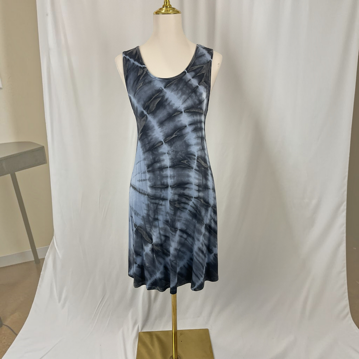 A sleeveless scoop-neck dress with a blue and gray tie-dye pattern displayed on a mannequin torso against a white fabric backdrop.