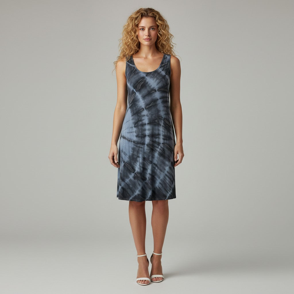 A woman modeling a sleeveless A-line dress with a blue and gray spiral tie-dye pattern, standing against a neutral light gray studio background.