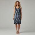 A woman modeling a sleeveless A-line dress with a blue and gray spiral tie-dye pattern, standing against a neutral light gray studio background.