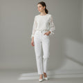 A woman modeling a white long-sleeve blouse with sheer lace sleeves and white straight-leg jeans, standing against a neutral gray studio background.