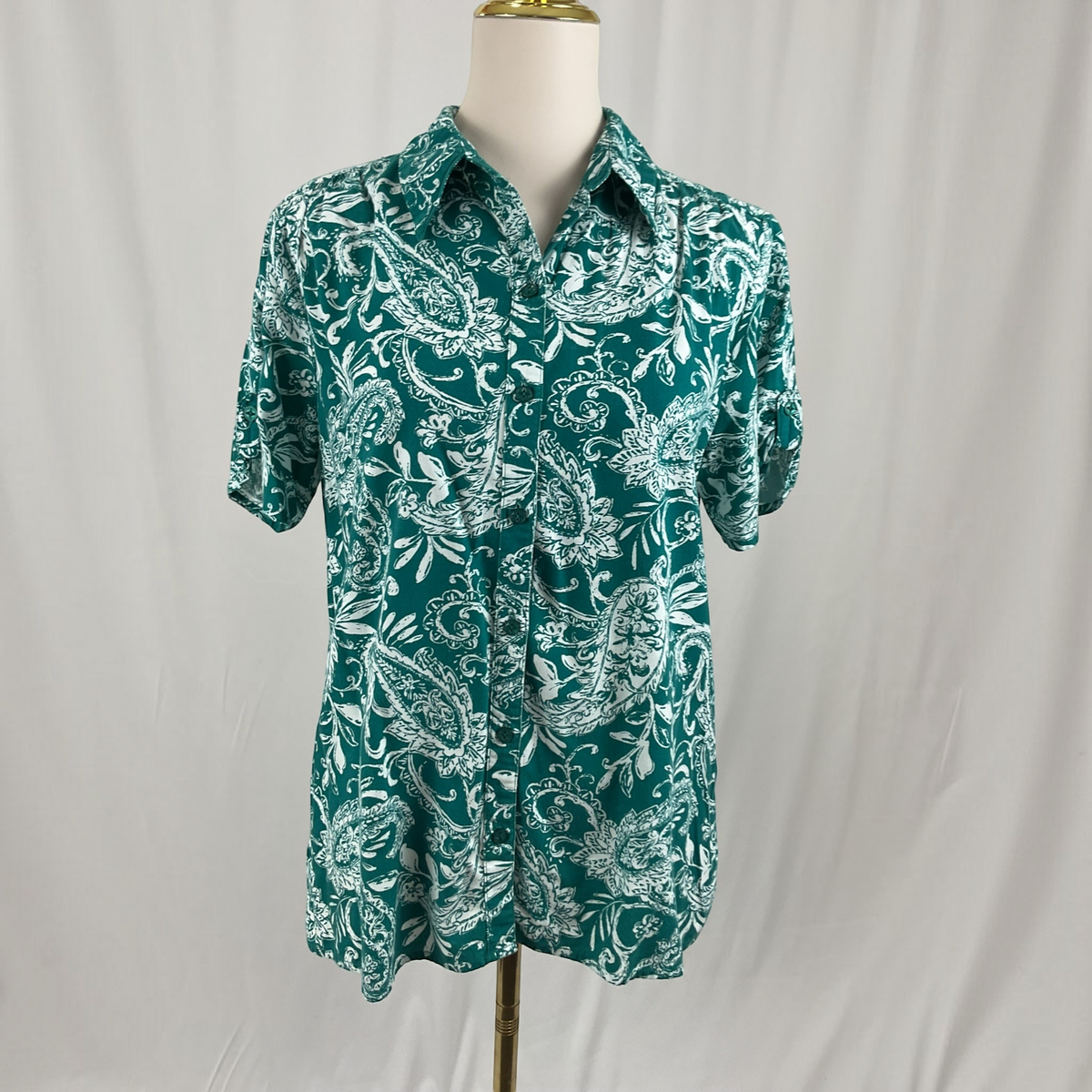 A woman with a floral print shirt, white jeans, teal sandals on a studio gray background