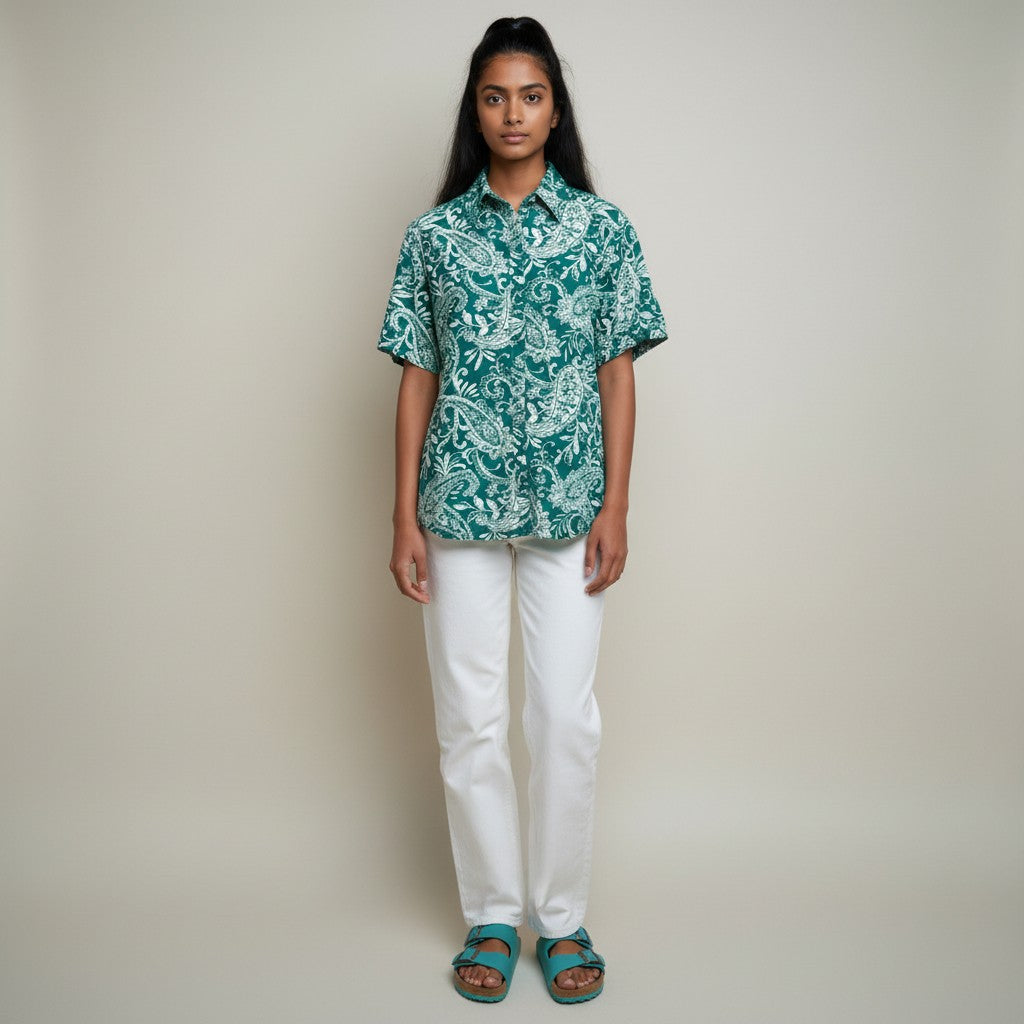 A woman with a floral print shirt, white jeans, teal sandals on a studio gray background