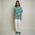 A woman with a floral print shirt, white jeans, teal sandals on a studio gray background