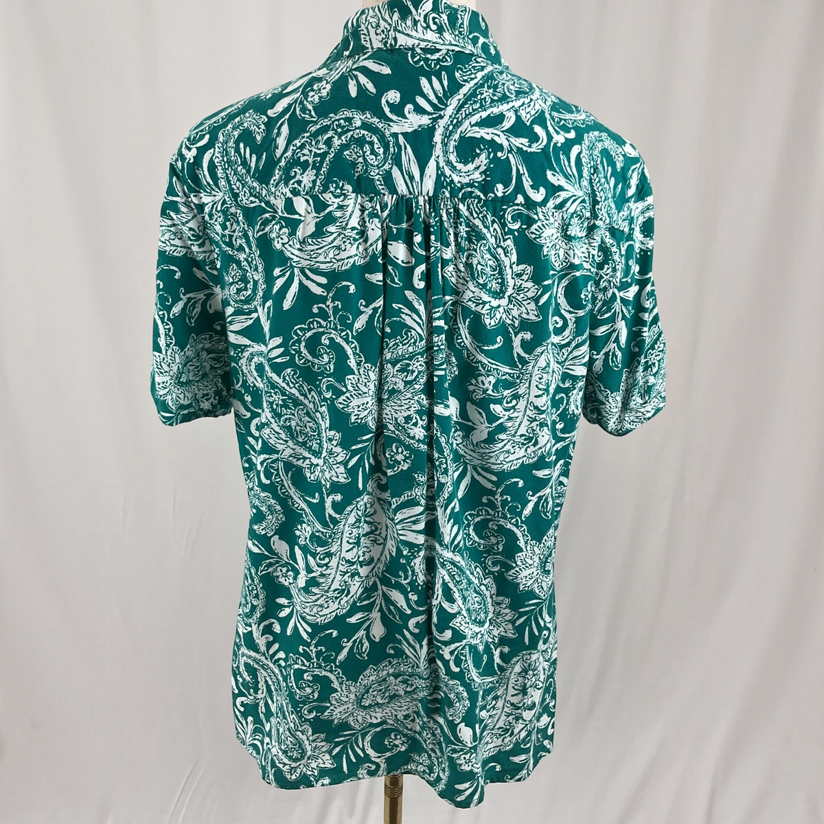 A woman with a floral print shirt, white jeans, teal sandals on a studio gray background