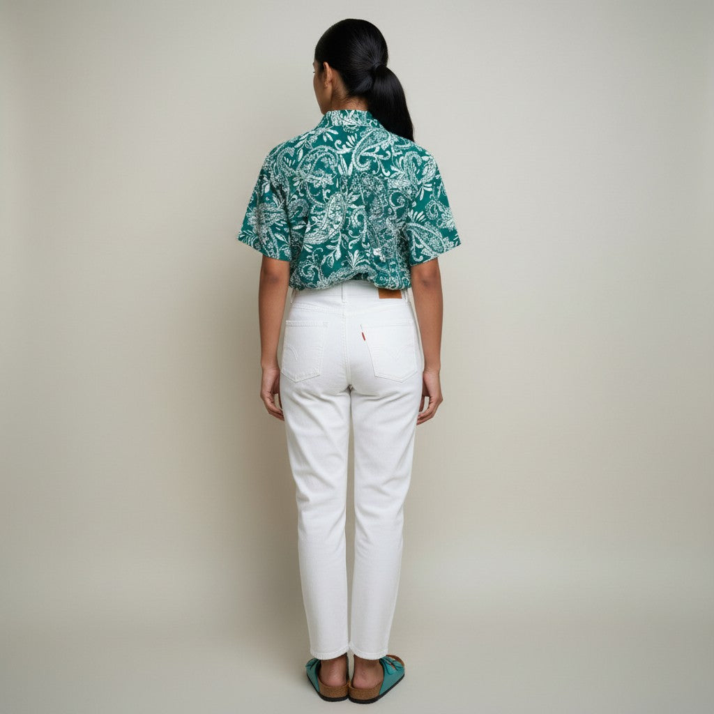A woman with a floral print shirt, white jeans, teal sandals on a studio gray background