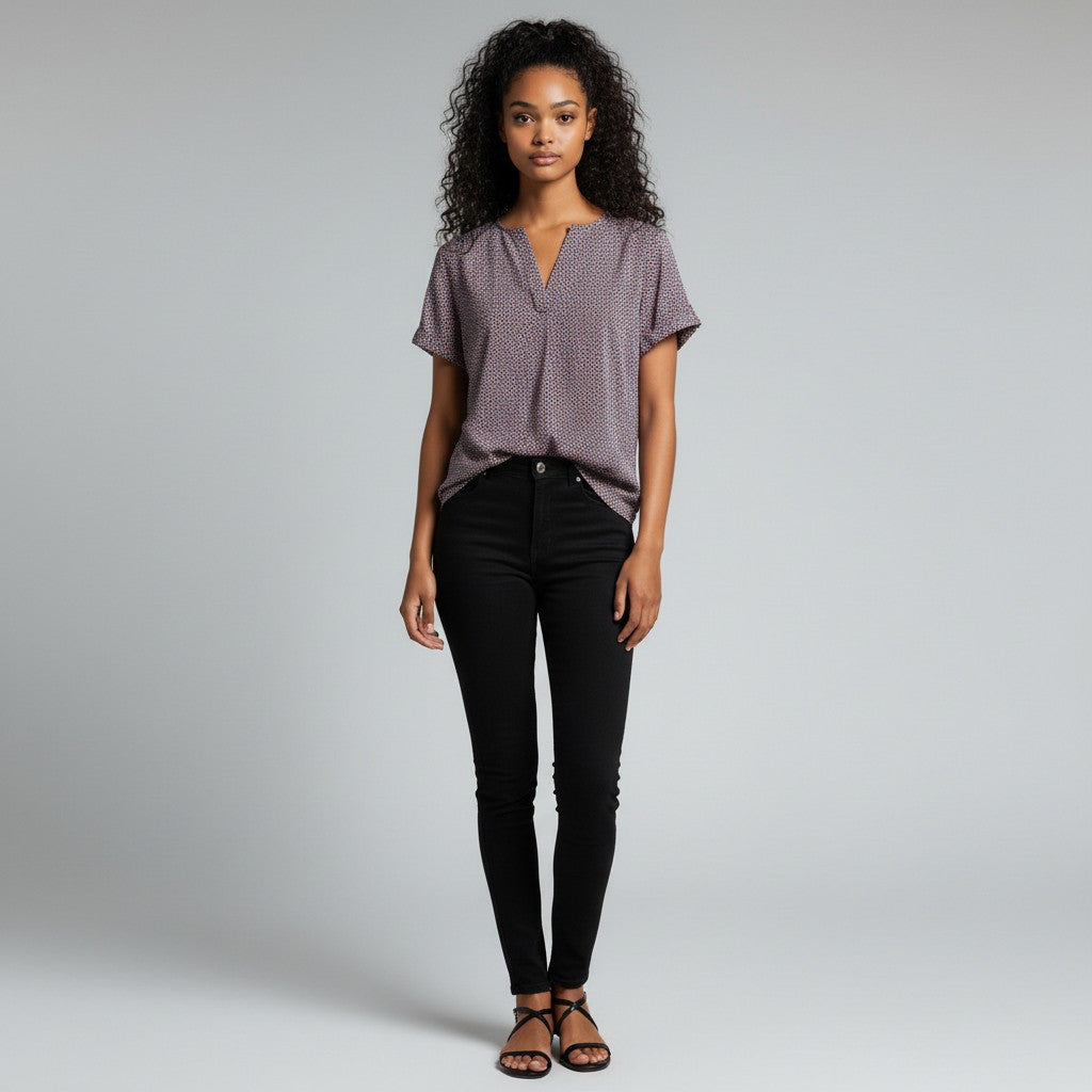 A woman wearing a dotted shirt, black jeans, black sandals on a studio gray background.