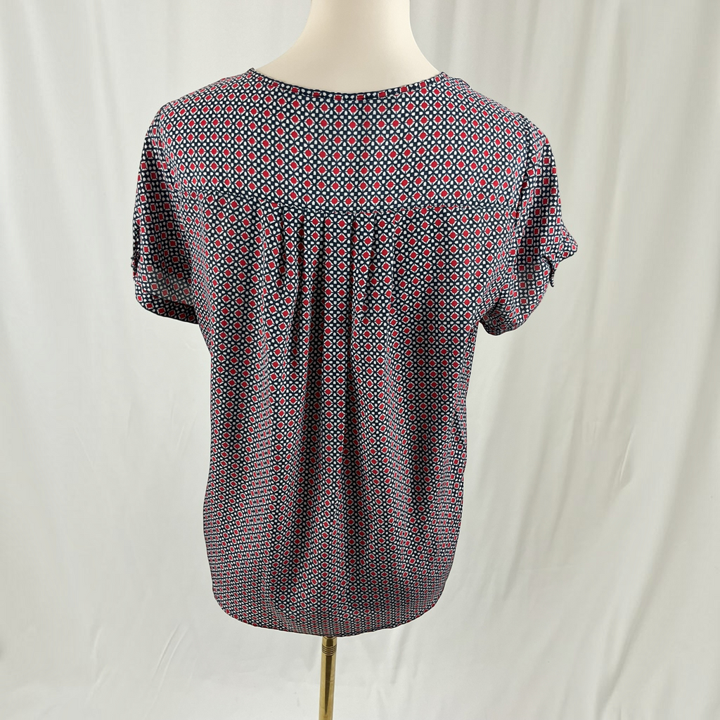A woman wearing a dotted shirt, black jeans, black sandals on a studio gray background.