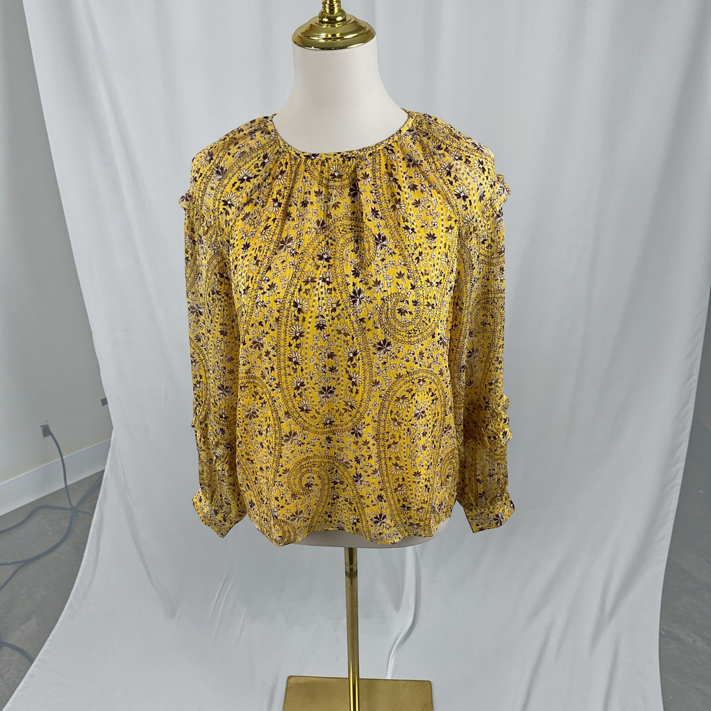 A yellow long-sleeve blouse with a dark paisley pattern, displayed on a cream dress form with a gold stand against a white fabric backdrop.