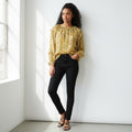 A woman is shown from the back wearing a yellow floral long-sleeve blouse and black pants against a light gray studio background.