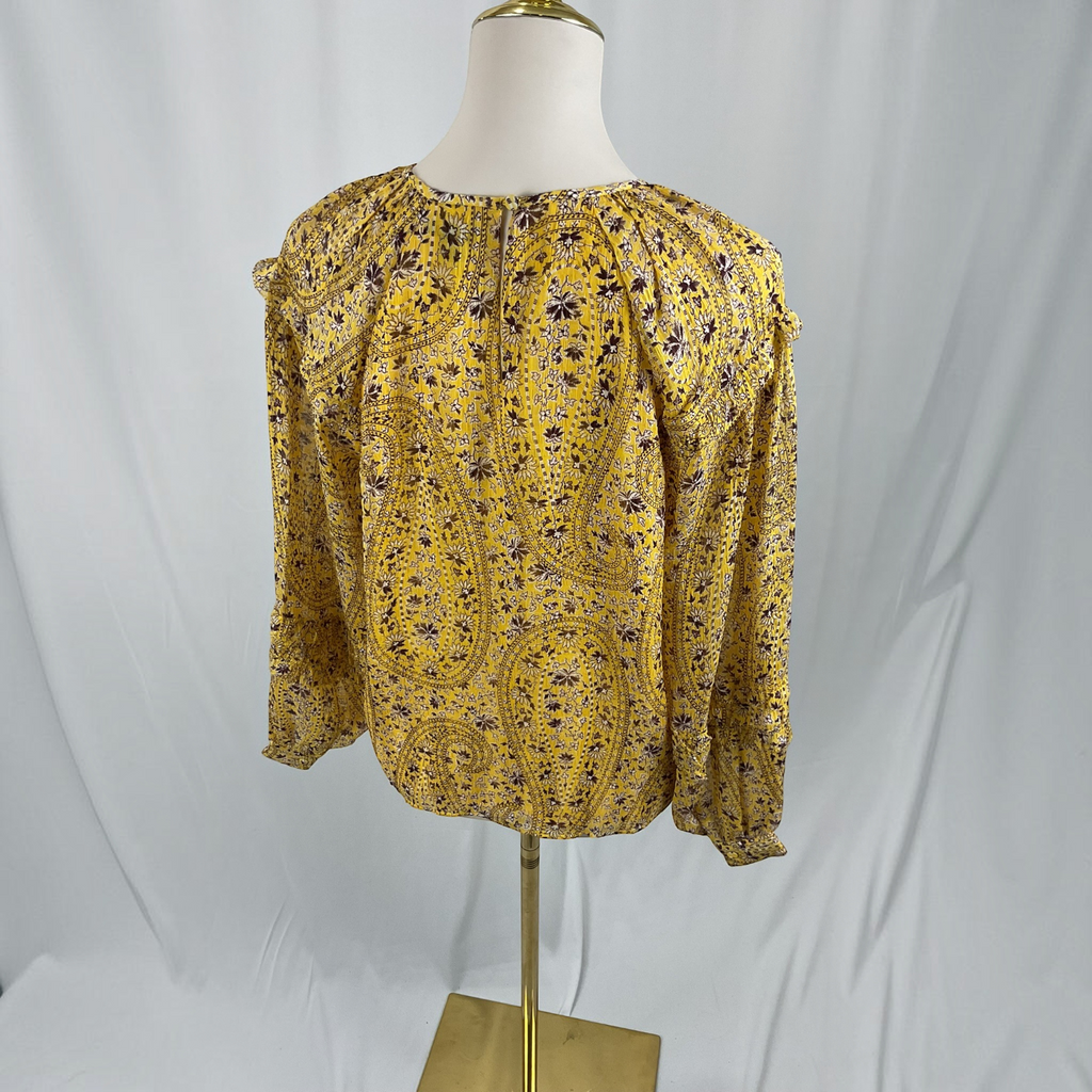 A woman is shown from the back wearing a yellow floral long-sleeve blouse and black pants against a light gray studio background.