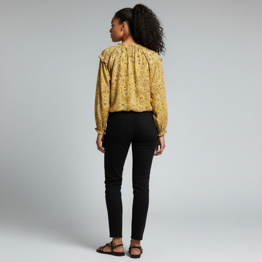 A woman is shown from the back wearing a yellow floral long-sleeve blouse and black pants against a light gray studio background.