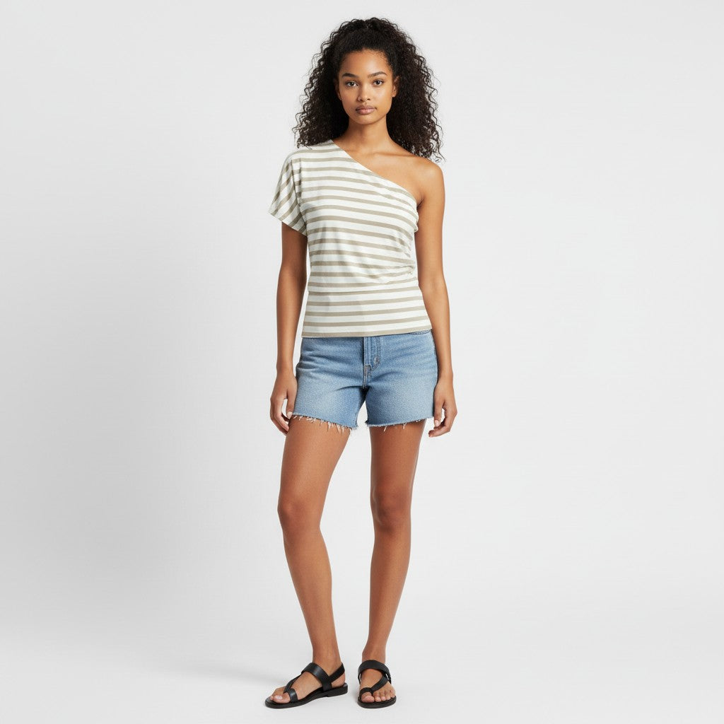 A woman wearing a strip asymmetrical t-shirt, jean shorts, black sandals on a studio gray background. 
