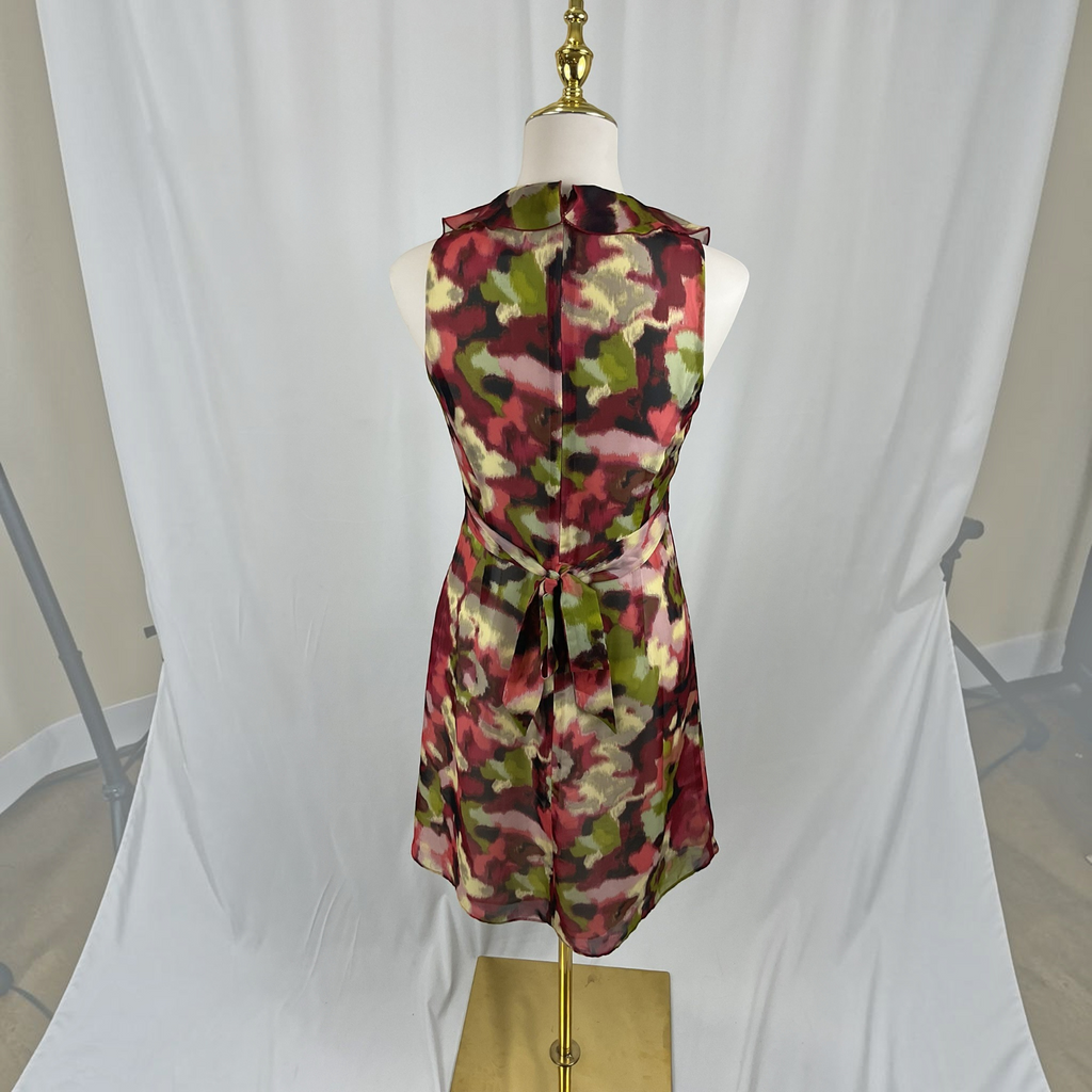 A sleeveless halter-neck dress with a tie waist, featuring a multicolor abstract floral pattern in red, green, pink, and beige, displayed on a mannequin against a white draped backdrop.