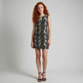 A sleeveless mini dress with a black and beige snakeskin pattern, worn by a model with red hair and black strappy heels against a light gray studio background.