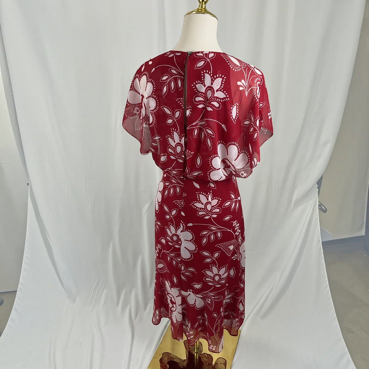 A red midi dress with a white floral pattern, displayed on a mannequin from the back. The dress features short flutter sleeves and a fitted waist, set against a white studio backdrop.