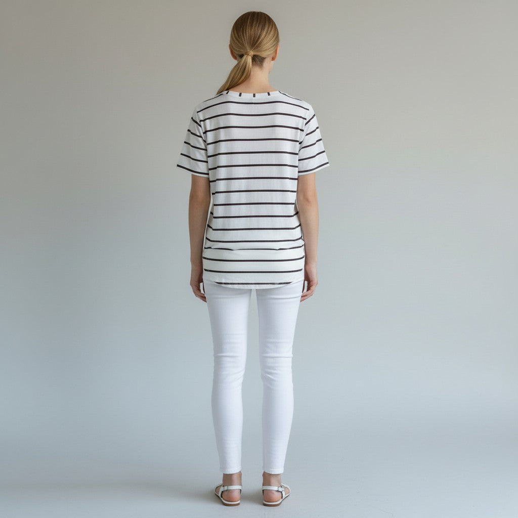 A woman viewed from behind wearing a white short-sleeve T-shirt with thin black horizontal stripes, paired with white pants and sandals, against a light gray studio background.