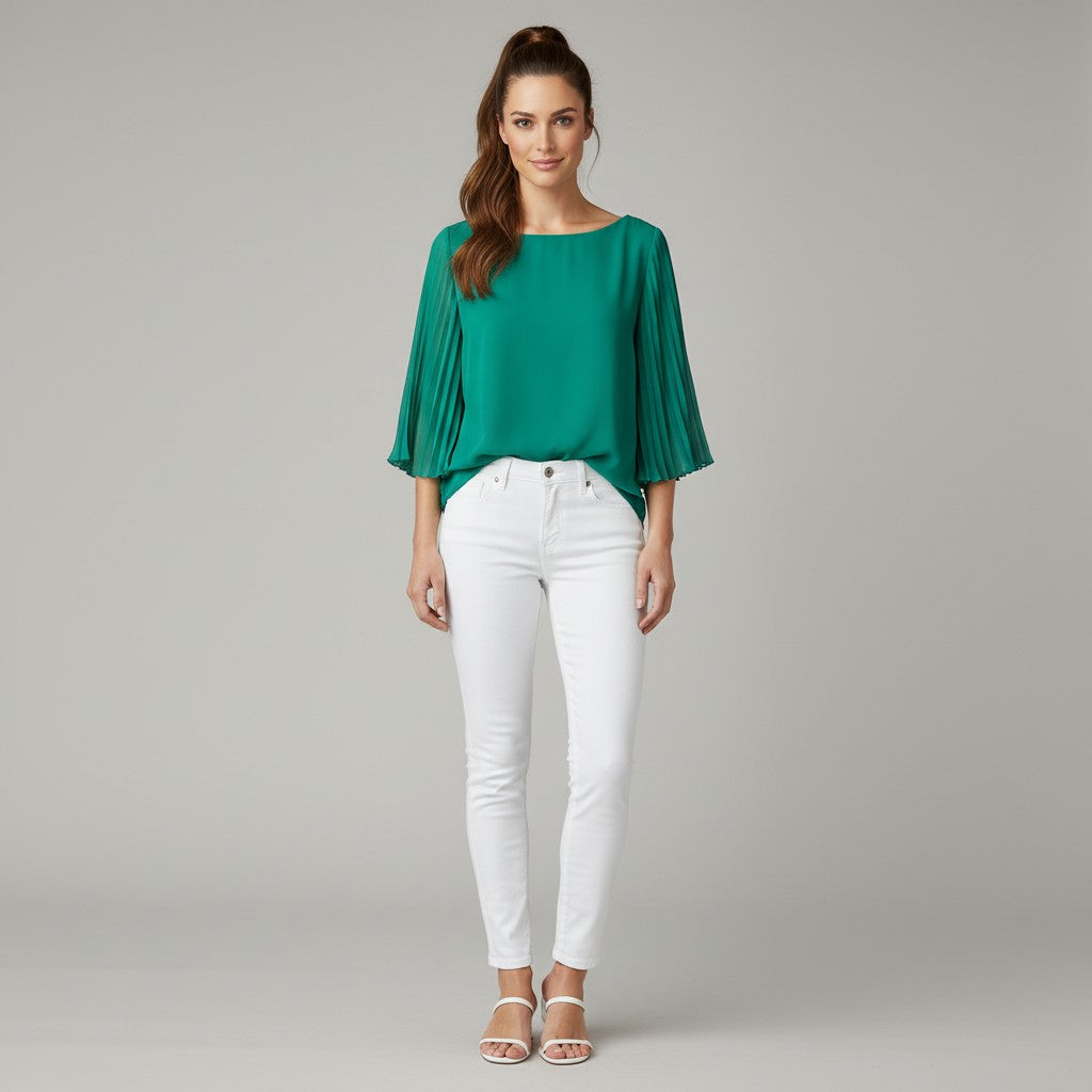 A woman modeling a vibrant green pleated three-quarter sleeve top paired with white skinny jeans and white heeled sandals, standing against a neutral gray studio background.