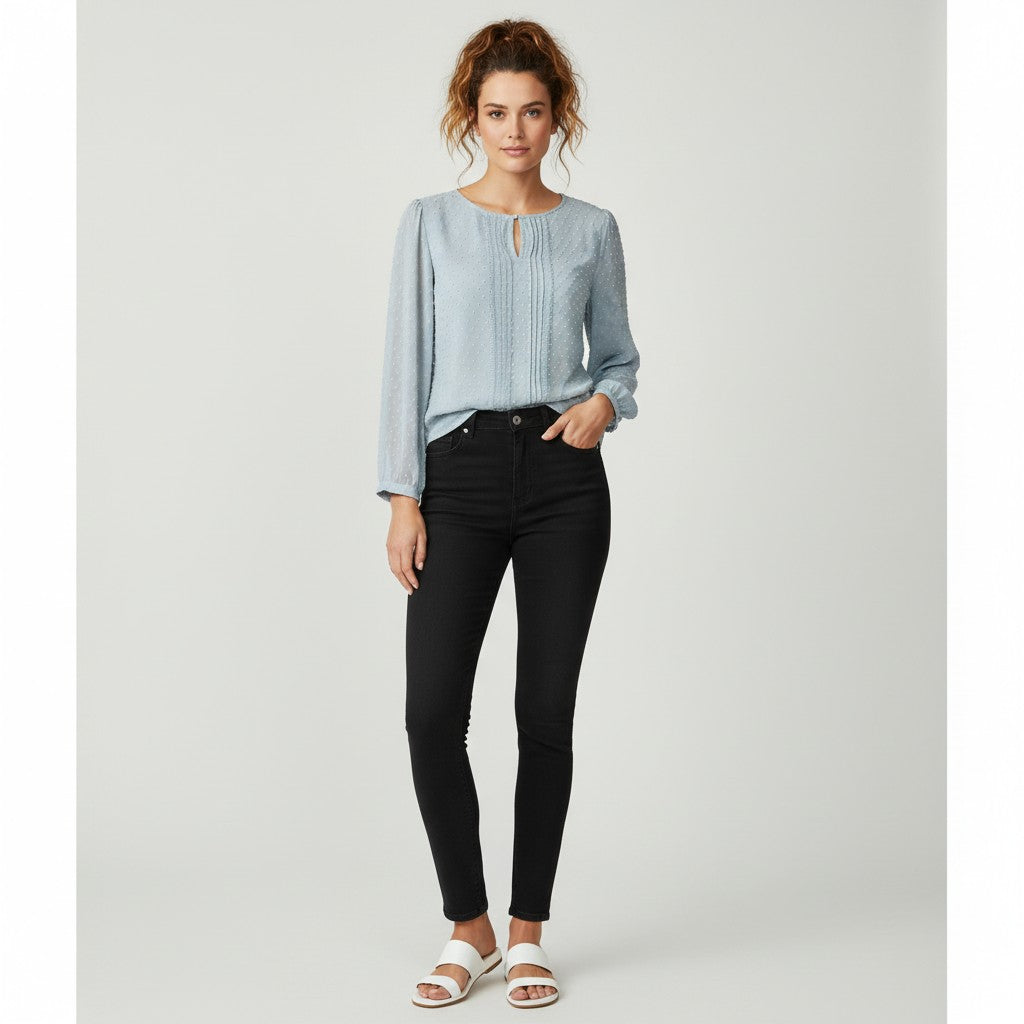 A woman modeling a light blue long-sleeve blouse with a keyhole cutout and black skinny jeans, standing against a light gray studio background.