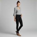 A woman modeling a light gray long-sleeve blouse with a keyhole cutout and flared sleeves, paired with black skinny jeans and brown strappy sandals, against a solid gray studio background.