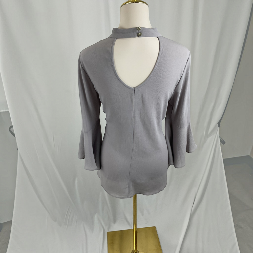 A light gray three-quarter sleeve top with a keyhole cutout at the neck, displayed on a mannequin torso with a gold stand against a draped white fabric backdrop.