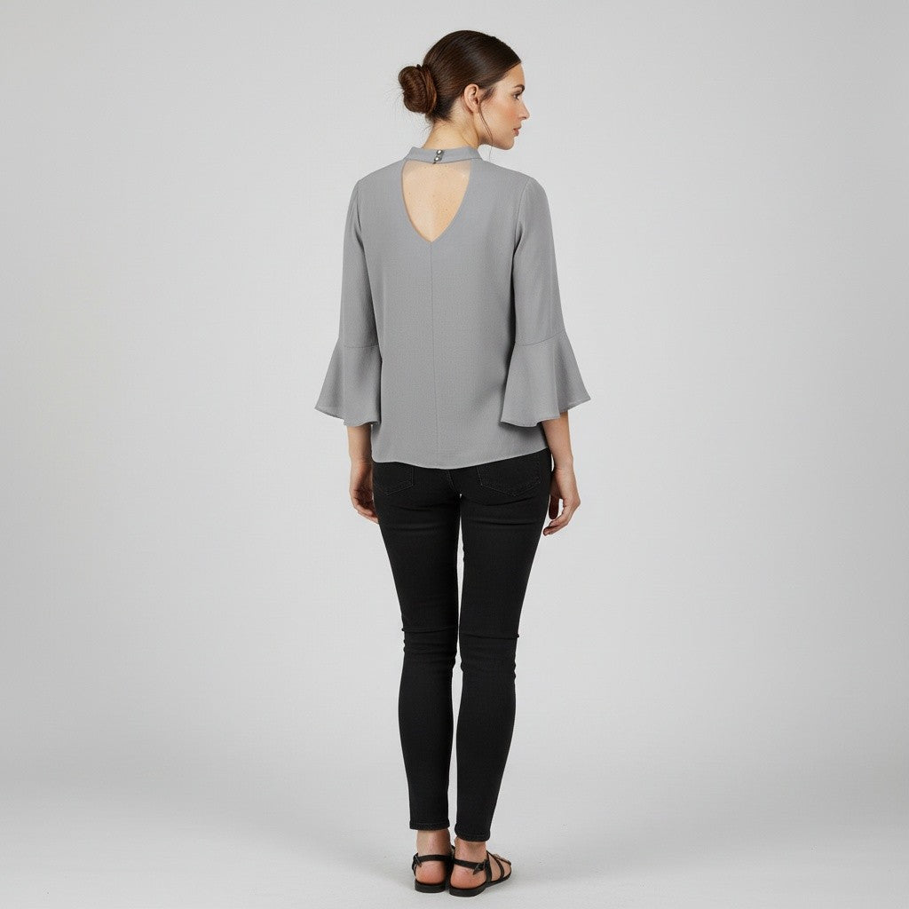 A woman shown from the back wearing a light gray blouse with a keyhole cutout and flared three-quarter sleeves, paired with black skinny pants and black sandals, against a light gray studio background.